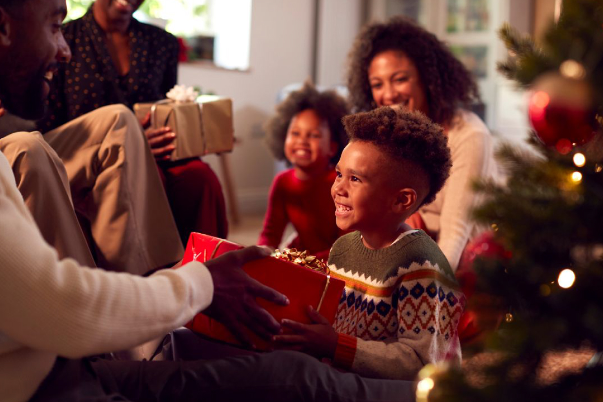 A child beams with joy as they receive a beautifully wrapped gift from an adult, surrounded by loved ones and the warm glow of a festively decorated Christmas tree--capturing the spirit of giving that makes holiday fundraisers so meaningful for families and communities.